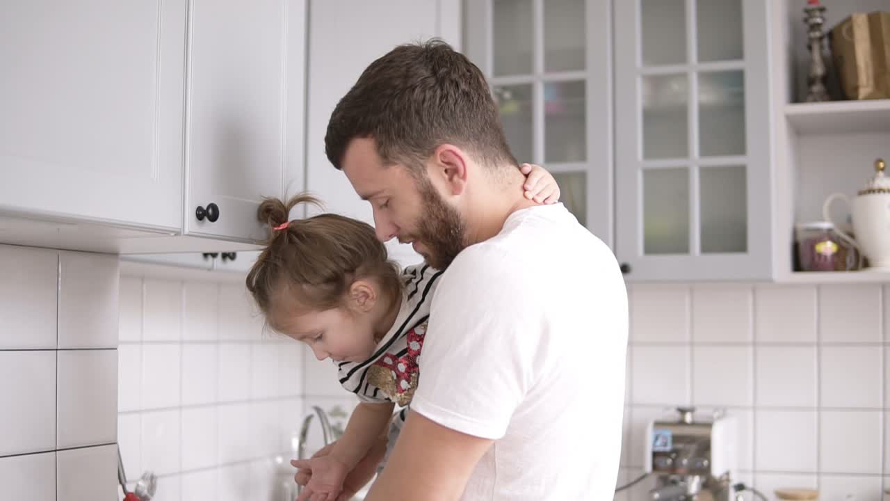 papá sostiene a una hija pequeña en sus brazos en la cocina