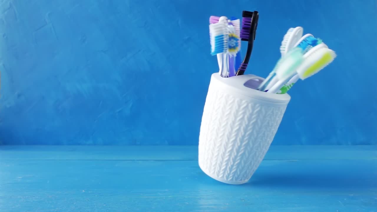 muchos cepillos de dientes diferentes en una taza blanca giran en una mesa contra un fondo azul. video de bucle crudo creativo 4k con efecto de rampa de velocidad. filmado en cámara de cine de alta velocidad, 1000 fps.