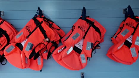 Orange-life-jackets-with-high-visibility-reflective-tape-hanging-on-a-blue-wall-ready-for-tourists-to-use-on-a-whale-watching-tour-boat