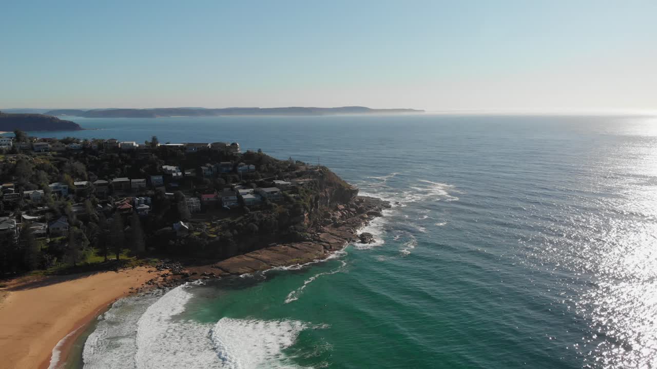 White sandy beach alongside rocky cliff, aerial fly over