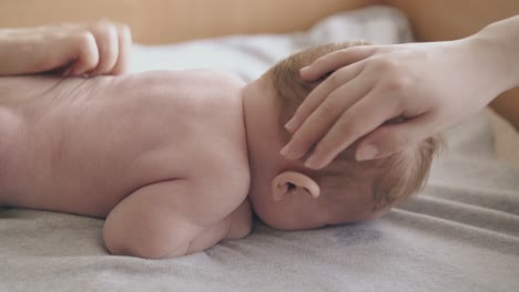 infant-boy-lies-on-changing-table-and-mother-pets-head