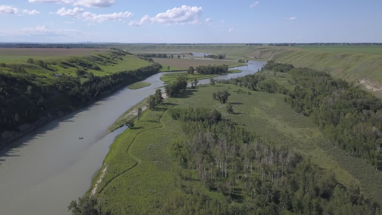 Una zattera solitaria galleggia su un bellissimo fiume della prateria, con una città all'orizzonte lontano.