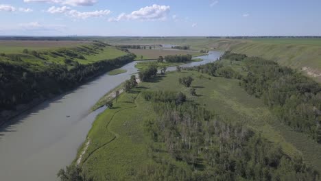 a lone raft floats on a beautiful prairie river, a city on the distant horizon