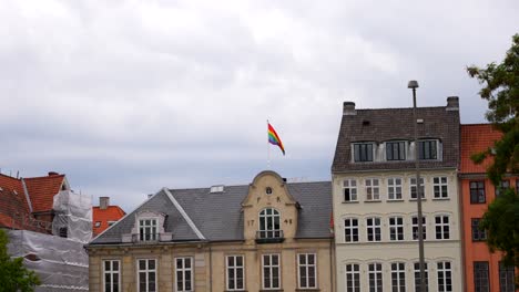 handheld shot of a lgbttqi+ flag waving on the top of an old building in copenhagen