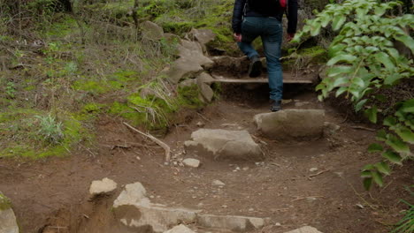 hombre fotógrafo excursionista con mochila y trípode caminando por un sendero subiendo unos escalones de piedra