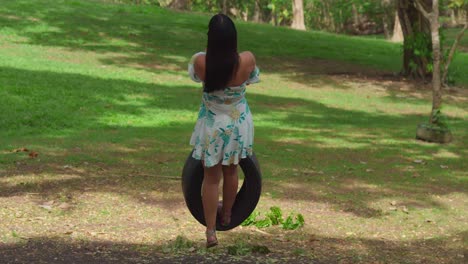 a girl swings on a tire in a short dress at a park on a sunny day in the caribbean