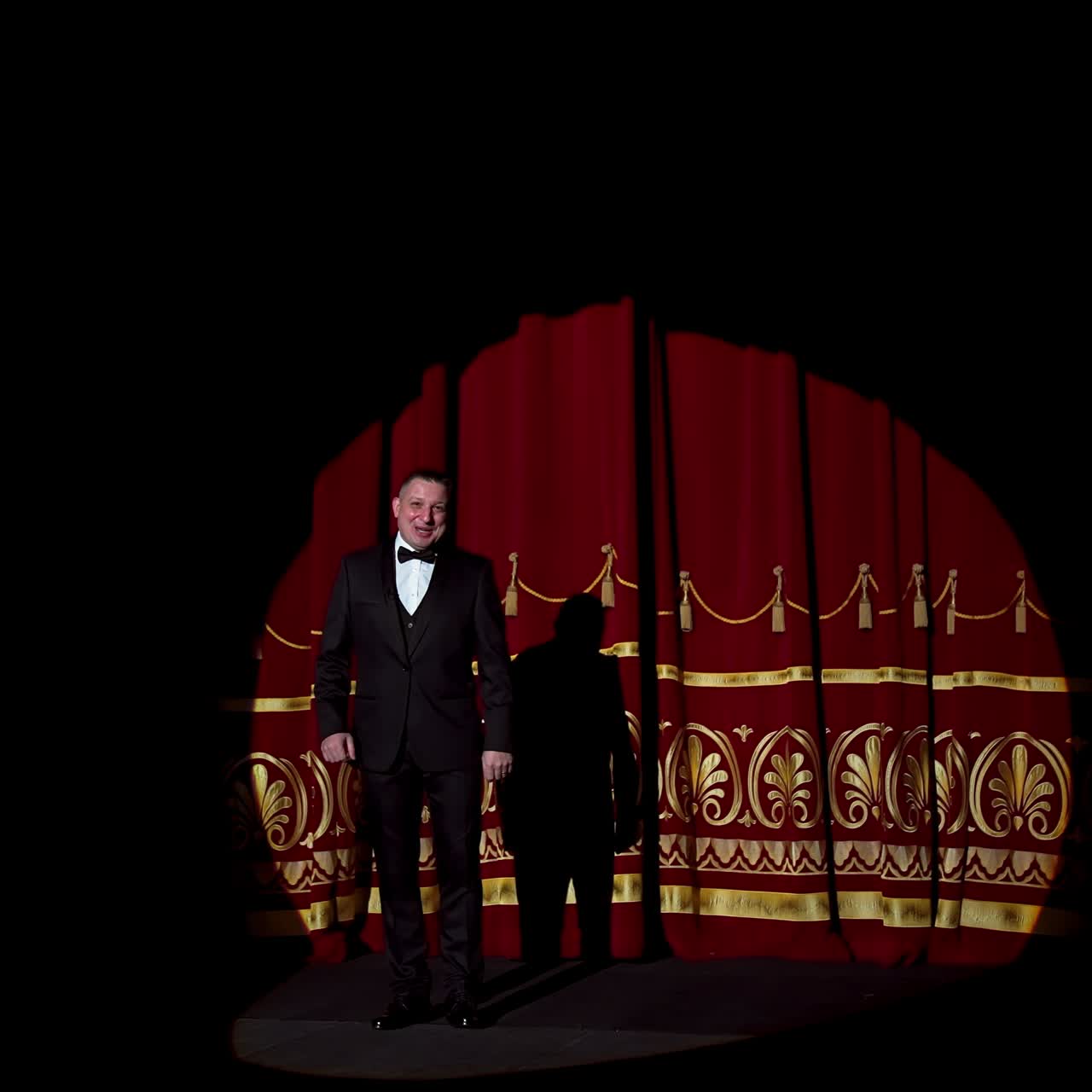 Announcer on a stage in theater. Bright round light on one person. man in black suit performs to the auditorium