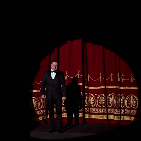 announcer on a stage in theater. bright round light on one person. man in black suit performs to the auditorium