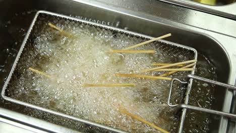 food being deep-fried on skewers in a commercial fryer