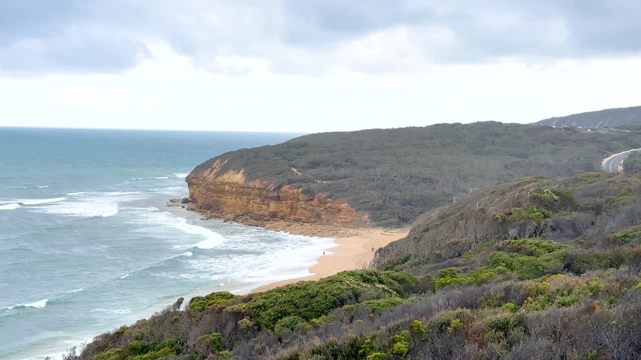 Aerial view of rugged coastline and ocean waves under cloudy skies along Great Ocean Road, Victoria, Australia