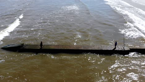 aerial video of two people fishing on the beach, one day with waves