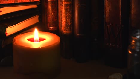 close up background of an ancient library, next to a frieplace, with old books, ink and a candle with flickering flame, with some dust flying around