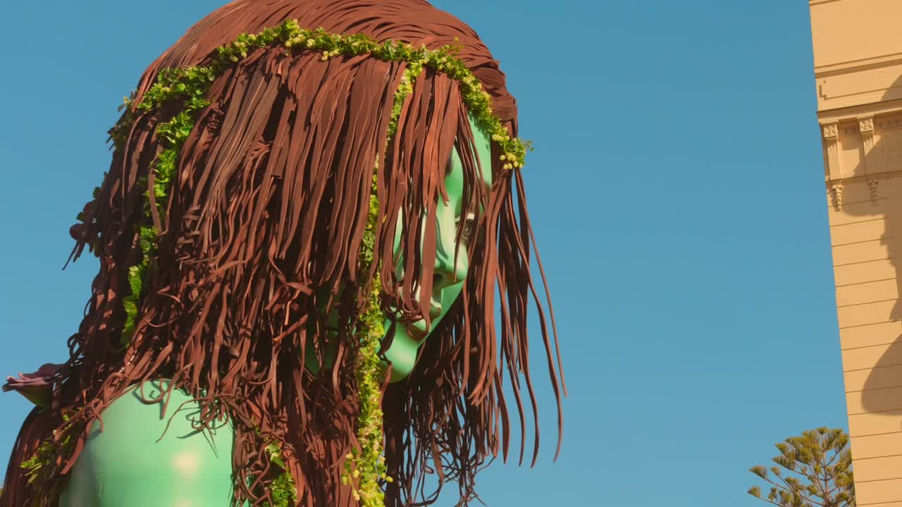 Grande statua di donna verde con ghirlanda di vite su sfondo di cielo blu