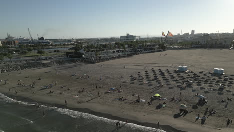 Drone-Video-of-a-Summer-Day-on-a-Beach-in-Valencia,-Spain-with-Two-Flags-in-the-Background