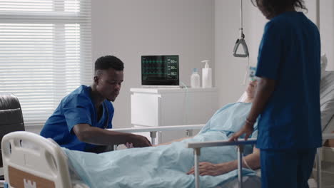 caring african ethnic medical team at the bedside of an elderly male patient. caring health care providers monitor vital signs of an elderly male hospital patient