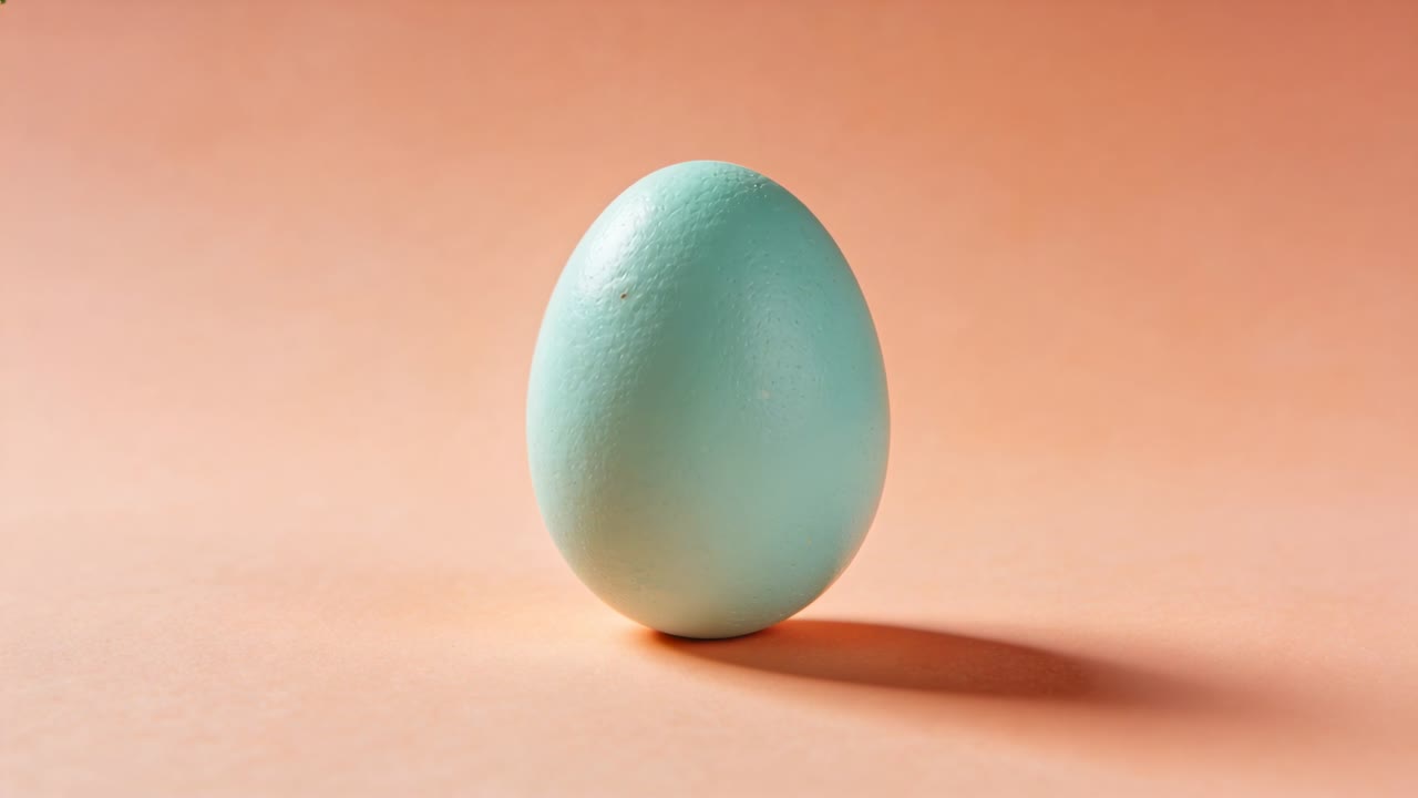 Shifting pale turquoise egg tilting and rolling after small shift on peach paper, moving shadow
