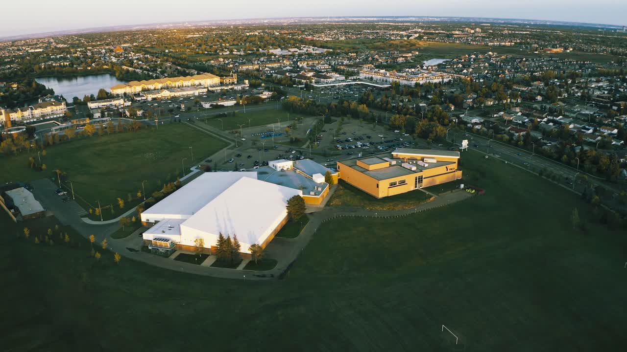 Aerial panaramic flyover massive community park facility with indoor recreational services and fitness areans, pools, rinks, excersize around a quiet outdoor grounds area birds eye view summer day 1-2