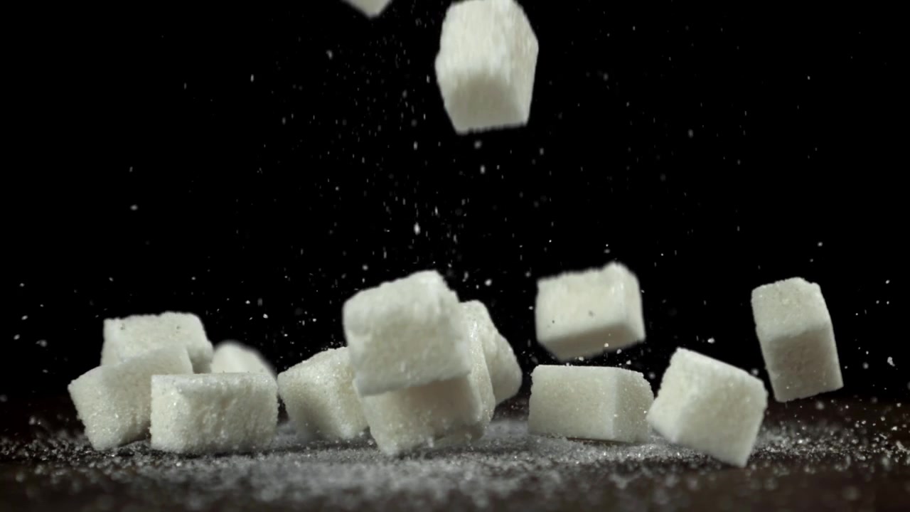Cubos de açúcar caindo e quicando em uma superfície escura em câmera lenta.