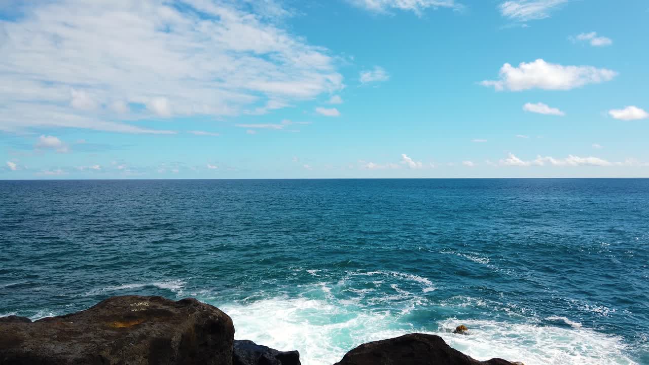 4K Hawaii Kauai boom up from dry and green grass and large lava rocks in foreground to ocean with partly cloudy sky