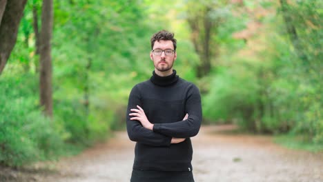 time lapse of a young caucasian man with a beard and glasses, dressed in a turtleneck sweater standing in an autumnal park, while passersby, people, and cyclists move and scurry around him