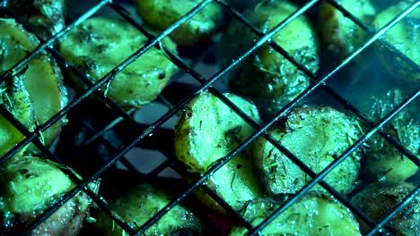 camera panning across closeup of browned herbed new potatoes in a wire basket on a hot grill with red embers glowing beneath