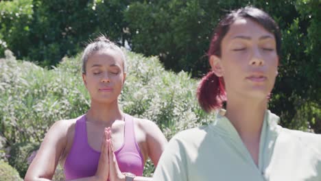 happy biracial sisters doing yoga and meditating in garden, in slow motion