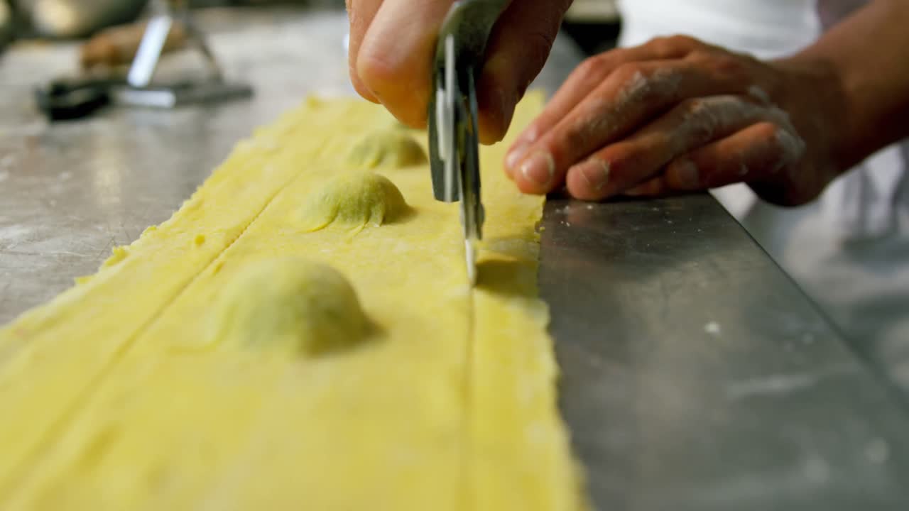 Male baker using pizza cutter on pasta dough in bakery shop 4k