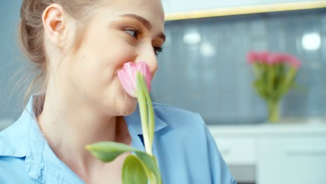 portrait of young blonde woman smelling flower in a kitchen.