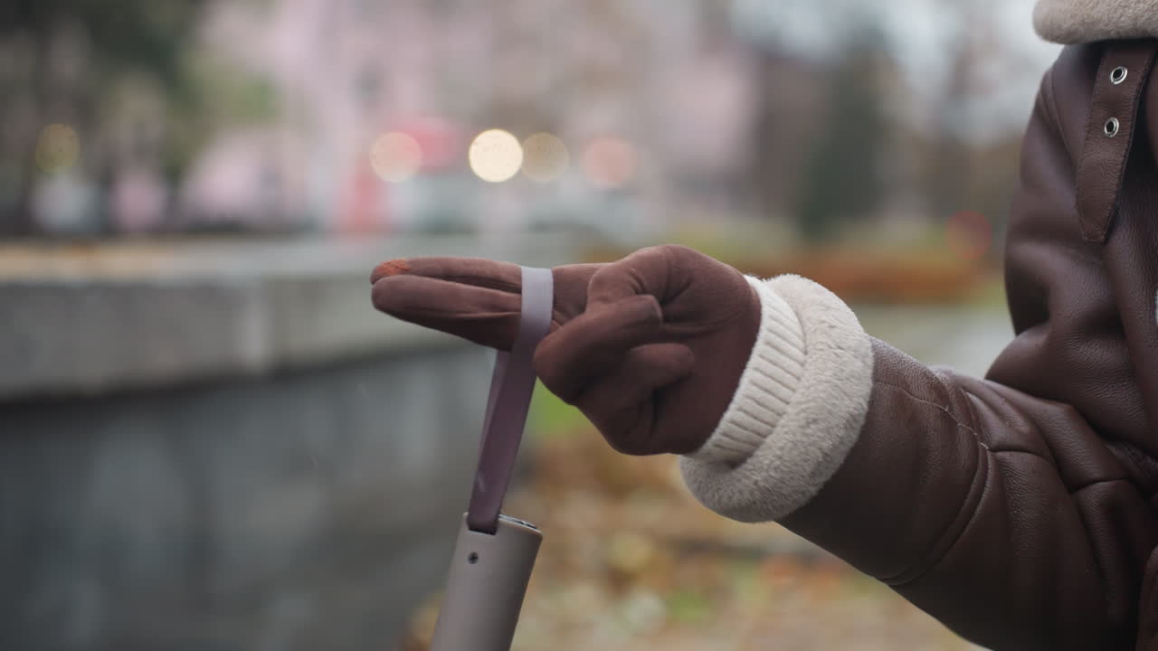 Close view of hand in brown glove and shearling jacket playfully swinging umbrella outdoors during cool autumn day with blurred city background and soft lighting capturing cozy seasonal vibes