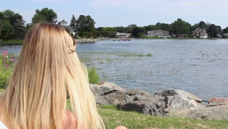 woman sits on coastline, looking towards harbor