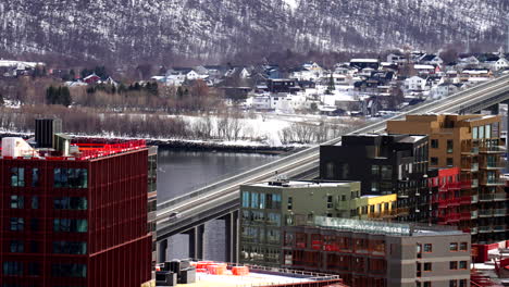 static establishing of cars driving across tromso bridge with arctic waters and snowy buildings in northern norway