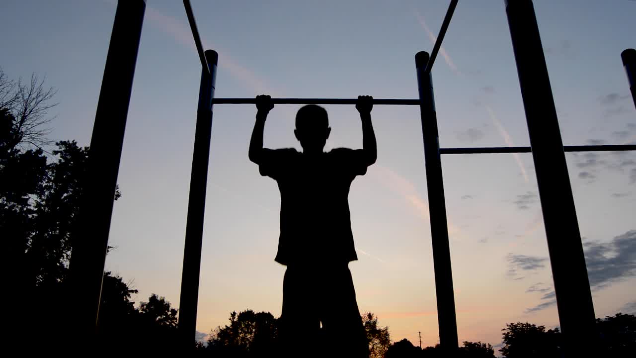 silueta masculina joven ejerciendo pullups antes del amanecer