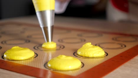 pastry chef is cooking macaroons. pouring dough on stencil silicone mat.