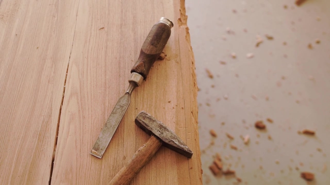 Nærbilde av stemjern og hammer som hviler på en trearbeidsbenk med trefliser etter utskjæring og meisling under trearbeidsprosessen i verkstedet.