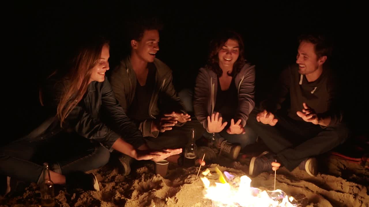 해변에서 불꽃에 앉아서 저녁에 손을 따뜻하게 하고, 얘기하고,