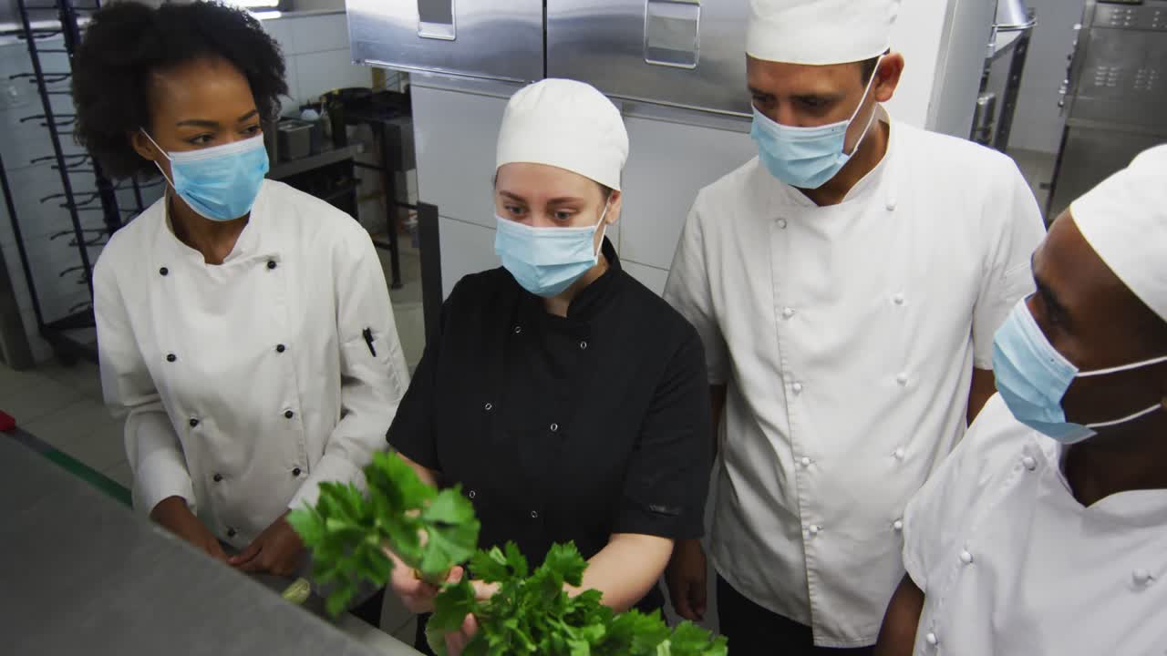 レストランの厨房でフェイスマスクを着用し、野菜を見ている様々な人種のシェフたち