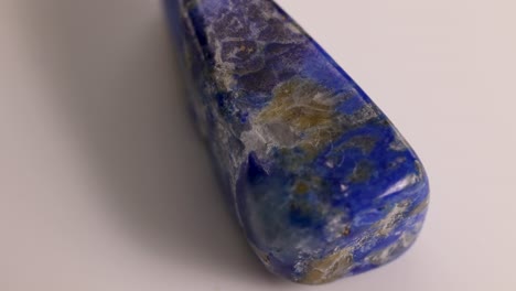 A lapis lazuli stone rotates on a white surface, showcasing its vibrant blue and gold hues under soft lighting