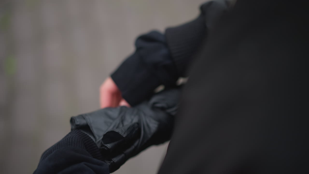 Mujer sosteniendo un paraguas cerrado sobre el hombro, perspectiva por encima del hombro, manga de chaqueta negra, pavimento mojado debajo, sutiles gotas de lluvia en la tela, estado de ánimo reflexivo, paso lento por la ciudad.