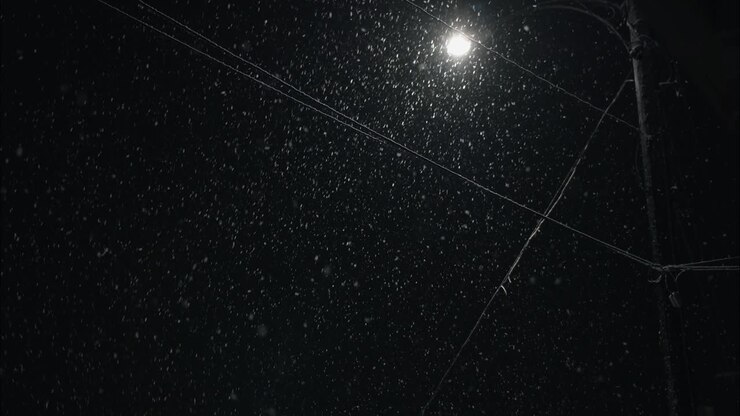 Winter snowfall at night snowing on city street in street light