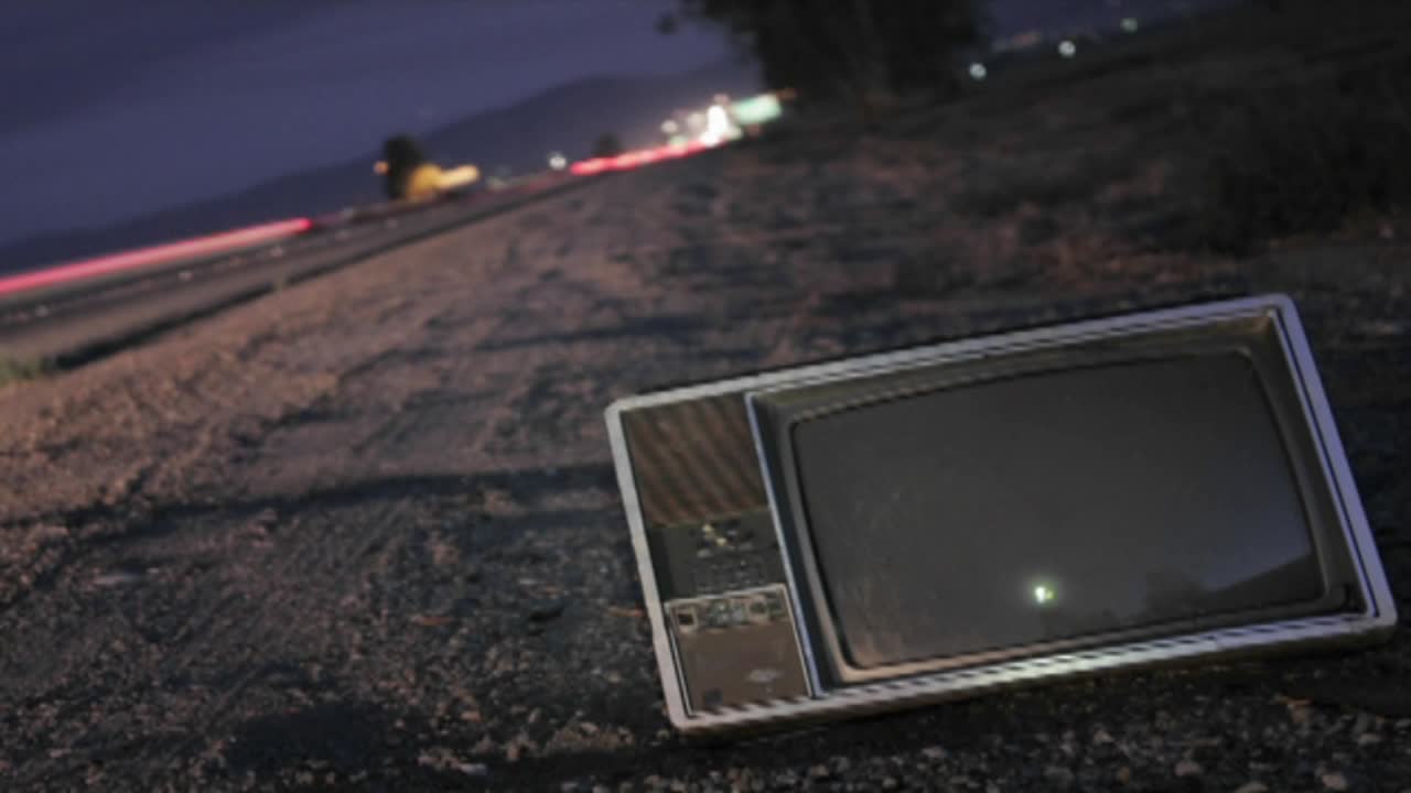 un televisor abandonado se sienta a lo largo de una carretera mientras el tráfico pasa en el lapso de tiempo
