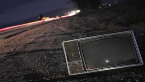 un televisor abandonado se sienta a lo largo de una carretera mientras el tráfico pasa en el lapso de tiempo