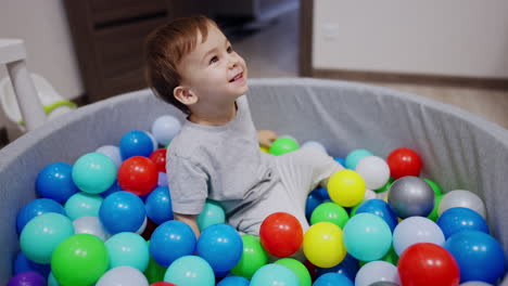 happy caucasian toddler falling into dry pool. smiling boy lies on balls and waves his feet actively.