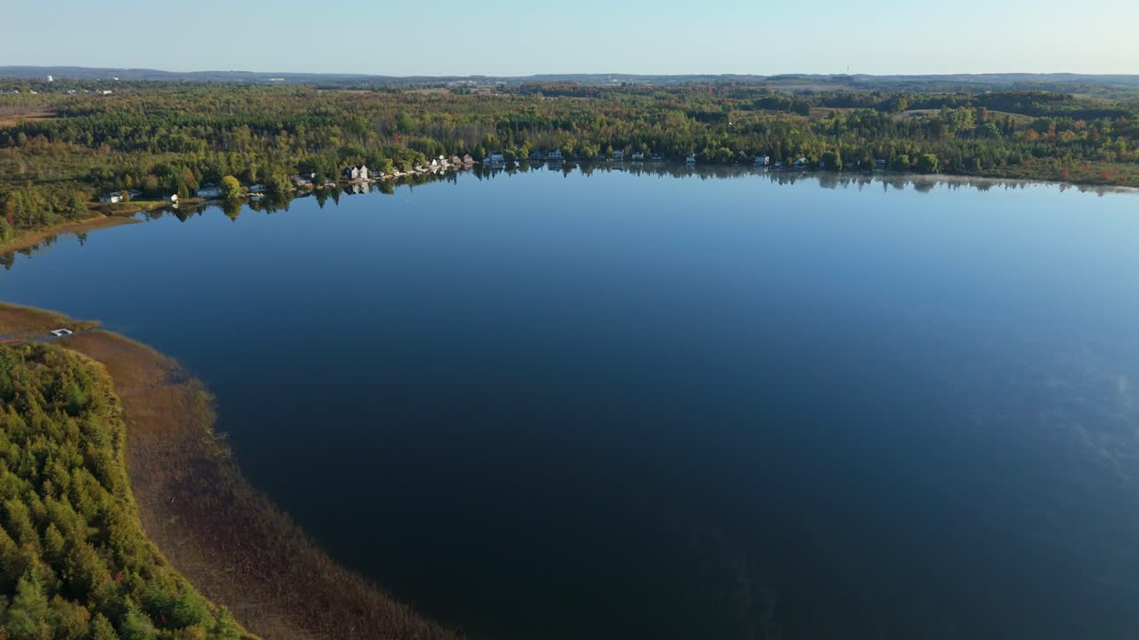 Drone push-in over autumn forest and deep blue Caledon Lake in Ontario