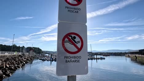 no fishing for fish and no bathing or swimming signs in the seaport located on the part of the water access with sunlight after sunrise, close-up shot traveling downwards