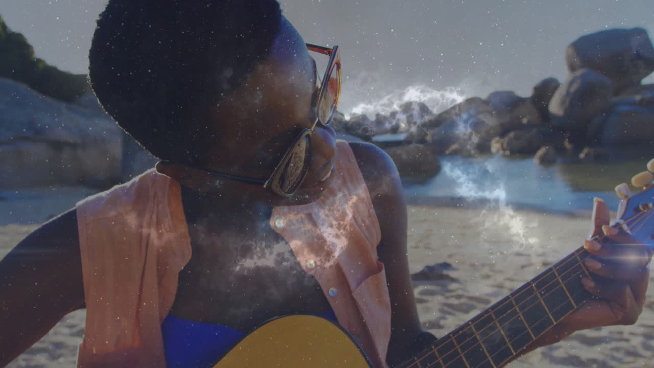 Musicista professionista che suona la chitarra sulla spiaggia con sovrapposizione di una nebulosa che appare, si illumina e svanisce per creare l'atmosfera
