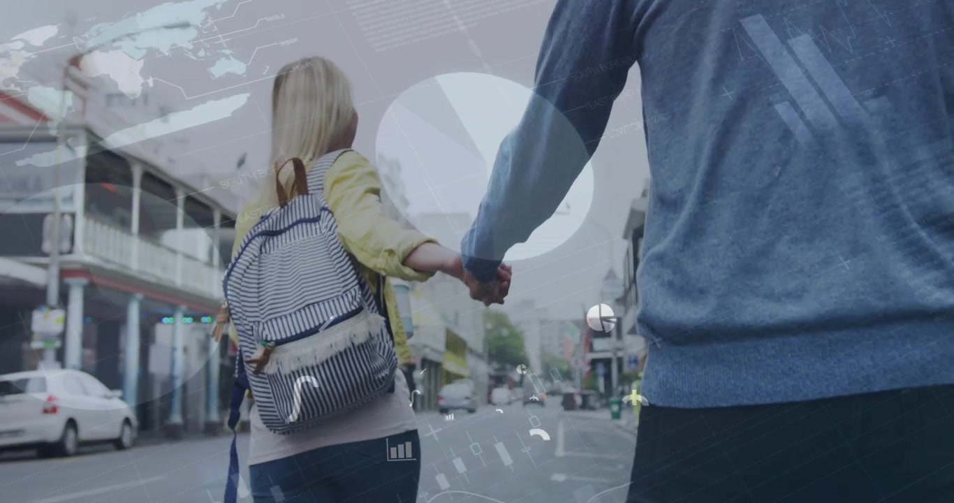 Una pareja caucásica camina por una ciudad, tomados de la mano y sonriendo.