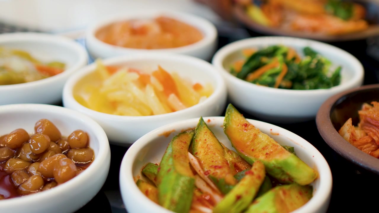 Bidikan statis jarak dekat berbagai lauk Korea fermentasi berwarna-warni yang tersusun di atas meja.