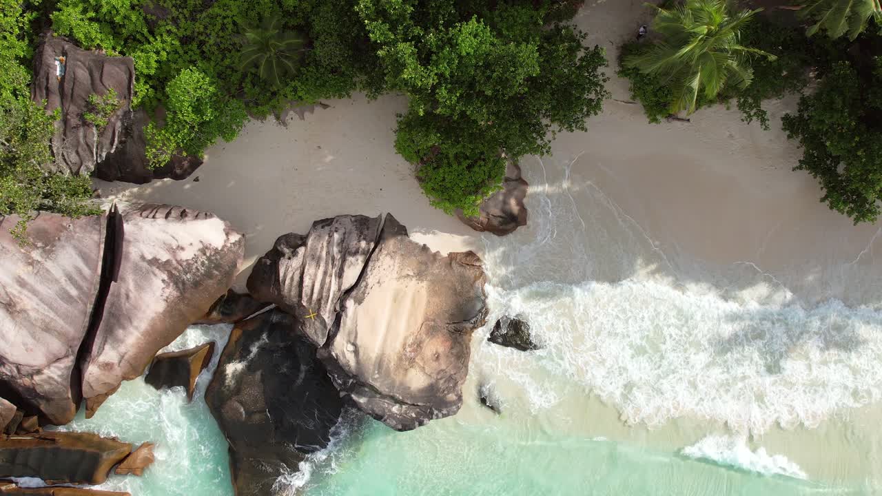Bird eye drone shot of white sandy beach, large granite stone, trees and waves crashing on the shore, Mahe Seychelles 60 fps 3