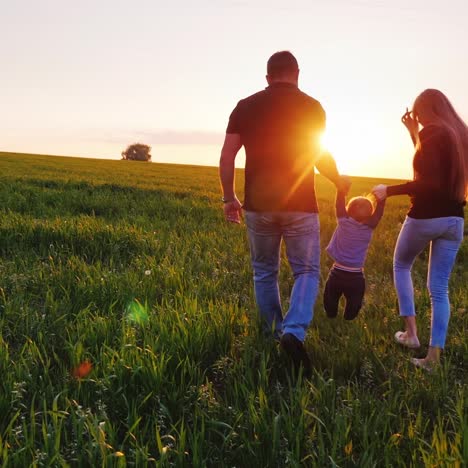 happy young parents are walking along the field the father is carrying the baby son in his arms