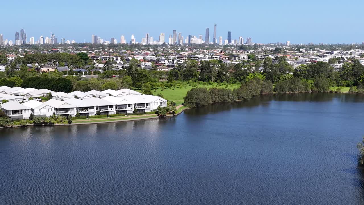 Drone pans across calm lake, waterfront homes, and distant city skyline under bright daylight